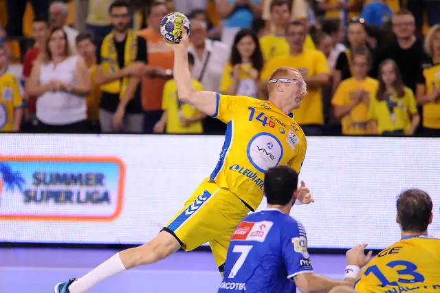 Piłkarz ręczny w żółtej koszulce z numerem 14 rzuca piłkę podczas eliminacji mistrzostw europy w piłce ręcznej grupa polska.