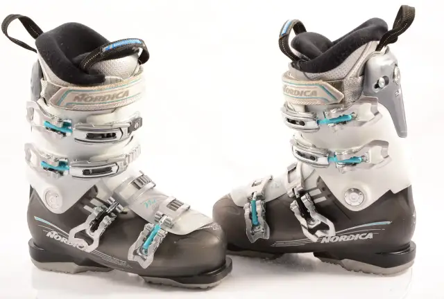 Botas de esquí Nordica para mujer, blancas y negras, con hebillas plateadas y detalles en azul.