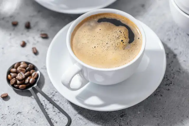Aromatic coffee in a white cup, with beans on a spoon. Czy kawa jest lekkostrawna? To zależy od sposobu parzenia.
