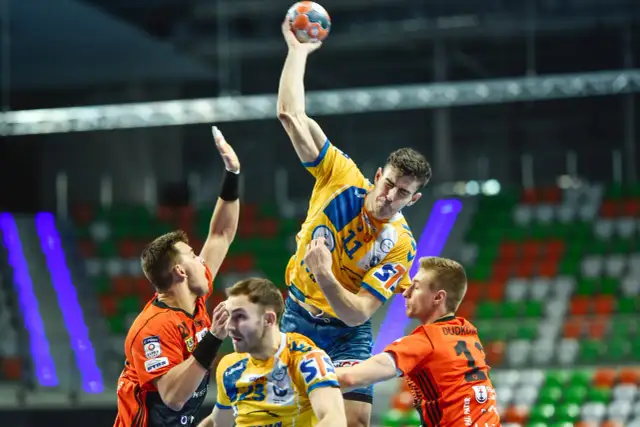 Gracz w żółtej koszulce rzuca piłkę do bramki, broniony przez zawodników w pomarańczowych strojach. Emocjonujący moment z meczu final four handball.