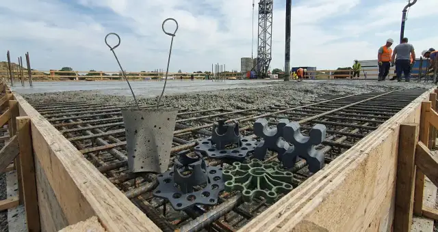 Na budowie widać zbrojenie i świeży beton. Na pierwszym planie leżą podkładki pod zbrojenie, które zapewnią odpowiednią grubość otuliny betonowej.