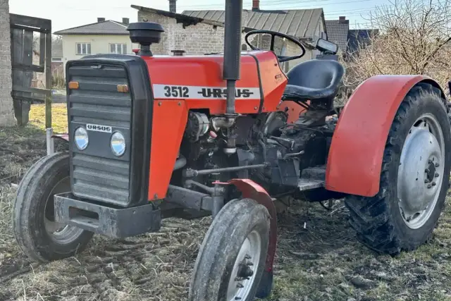 Czerwony ciągnik Ursus 3512 z czarną maskownicą i siedzeniem, stojący na ziemi.
