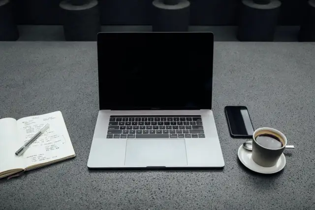 Laptop, notatnik, telefon i kawa na szarym blacie. Zastanawiasz się, ile wat pobiera laptop?