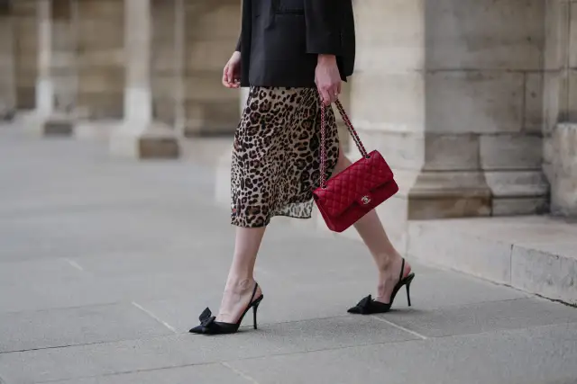 Elegancka kobieta w sukience w panterkę i czarnym blazerze, z czerwoną torebką Chanel. Czy sukienka w panterkę jest modna? Zdecydowanie tak!