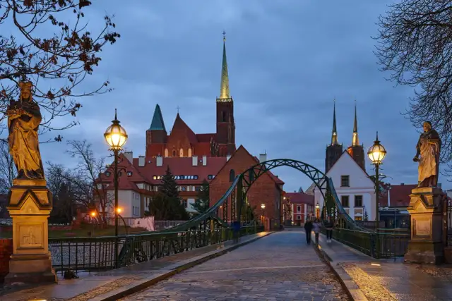 Most wrocławskiej katedry o zmierzchu z widokiem na wieże kościelne i rzeźby.