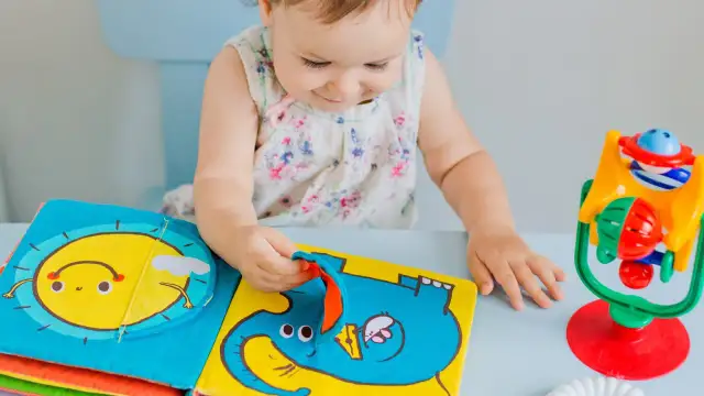 Dziecko bawi się kolorową książeczką sensoryczną z motywem słonia i słońca.