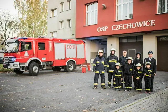 Strażacy OSP Czechowice z wozem strażackim i dziećmi w strojach strażackich.