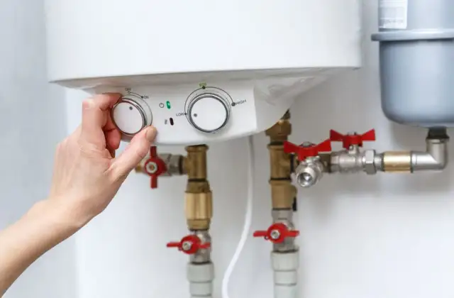 Dłoń kręci pokrętłem bojlera, przygotowując go do pracy. Widać zawory i rury, kluczowe elementy do tego, jak przepłukać bojler.