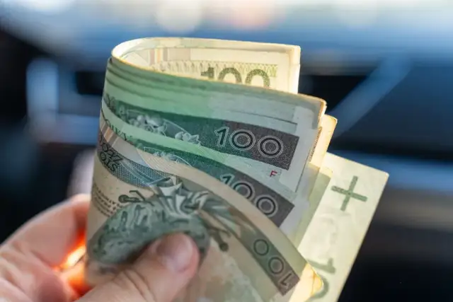 Dłoń trzyma banknoty 100 zł. Kiedy wypłata 13 i 14 emerytura 2026?