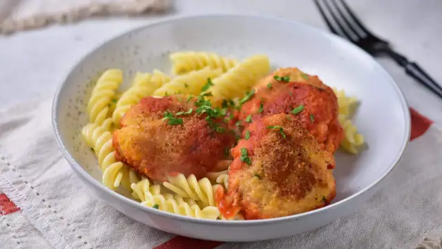 Kotlety w sosie pomidorowym z makaronem fusilli, posypane natką pietruszki.