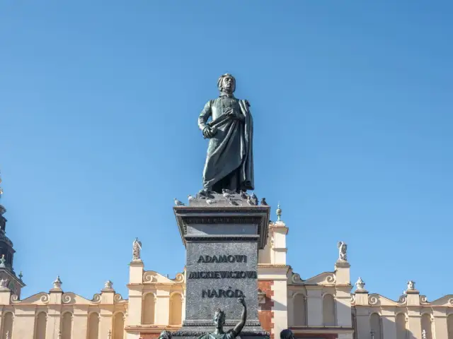 Pomnik Mickiewicza, symbol romantyczności, na tle Sukiennic. Streszczenie epoki w kamieniu i architekturze.