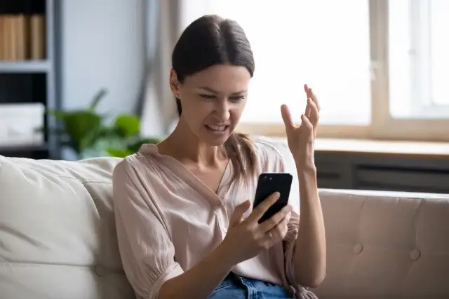 Femme frustrée sur son canapé, regardant son téléphone avec exaspération. Elle dit : "Je ne capte pas chez moi !