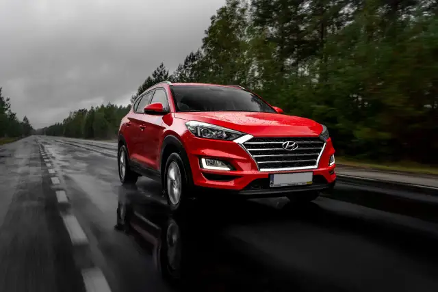 Czerwony Hyundai Tucson jedzie po mokrej drodze w deszczowy dzień. Warto pamiętać o filtrze CPL, którego zastosowanie poprawia widoczność w takich warunkach.