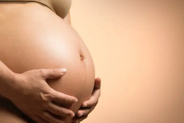 Brzuch kobiety w ciąży, delikatnie obejmowany dłońmi. To obraz nadziei i nowego życia, być może dla surogatki.