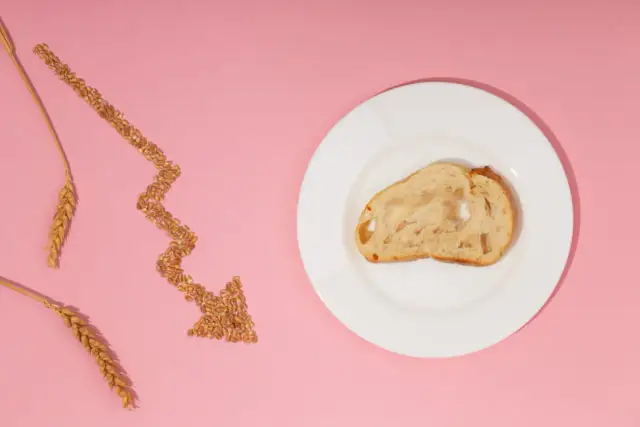 Strzałka z ziaren pszenicy wskazuje na kromkę chleba na talerzu, symbolizując uczulenie na gluten i potrzebę unikania go.