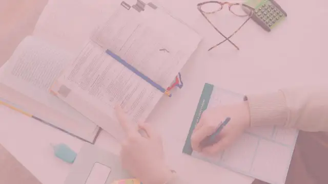Otwarta książka, ręka pisząca w notatniku, okulary i kalkulator.