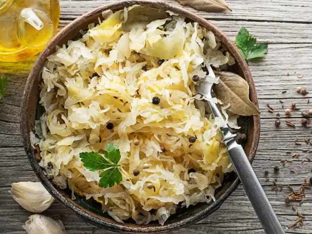 Miseczka pełna aromatycznej surówki z kiszonej kapusty, doprawionej pieprzem i kminkiem. Obok czosnek i buteleczka oleju.