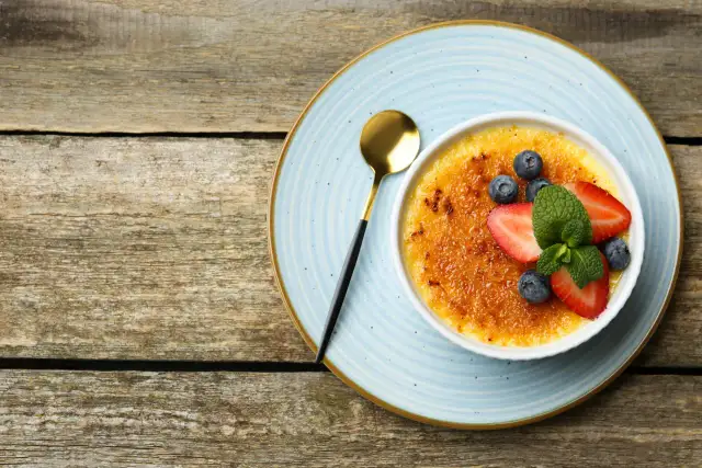 Idealny Crème Brûlée przepis na chrupiącą karmelizowaną skórkę i aksamitny krem. Udekorowany truskawkami, borówkami i miętą.