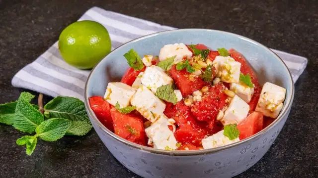 Erfrischender Wassermelone Feta Salat mit Minze und Pinienkernen, garniert mit Limettenabrieb. Ein leichter Genuss.