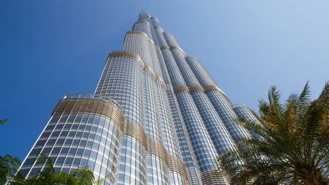 Burj Khalifa, najwyższy budynek na świecie, wznosi się ku błękitnemu niebu, otoczony palmami.