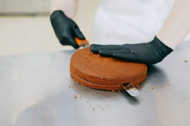 Manos enguantadas cortan un bizcocho redondo, preparándolo para ser la base de una deliciosa masa de tarta.