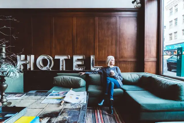 Kobieta z kawą siedzi na kanapie w hotelu. Zastanawia się, ile zarabia technik hotelarstwa.