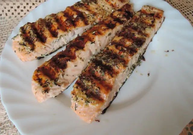 Trzy grillowane filety łososia, przyprawione ziołami, wyglądają apetycznie. Idealna marynata do lososia sprawia, że ryba jest soczysta i aromatyczna.