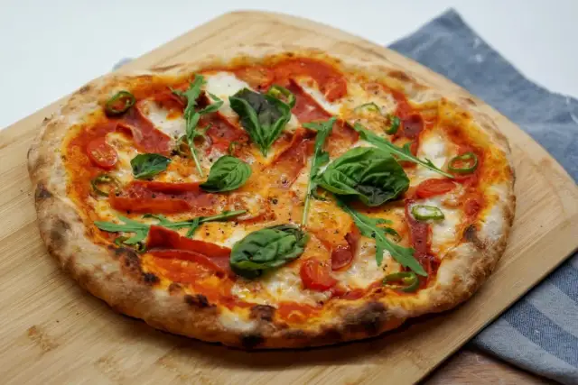 Pizza z pikantnym salami, pomidorkami, rukolą i bazylią na drewnianej desce.