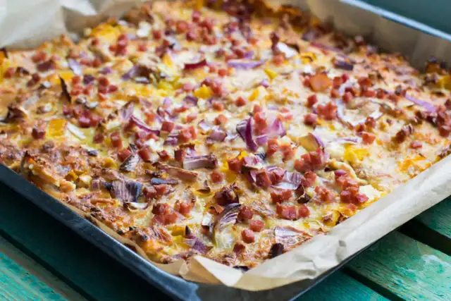 Herzhafte pizza ohne kohlenhydrate mit Speck und roten Zwiebeln, frisch aus dem Ofen auf Backpapier.
