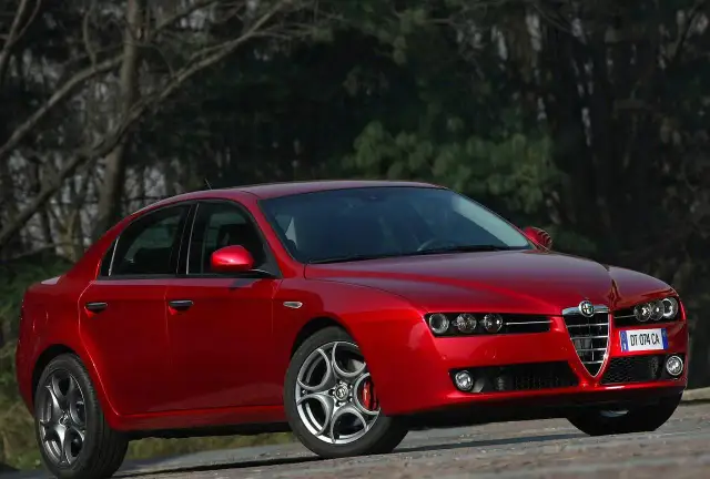 Czerwone Alfa Romeo 159 1.9 JTD z charakterystycznym grillem, zaparkowane na tle drzew.