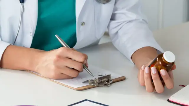 Lekarz rodzinny pisze receptę na leki na nerwicę, trzymając w dłoni buteleczkę z lekami.