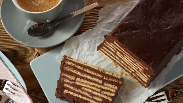 Schokoladiger kalter Hund, geschichtet mit Keksen, neben einer Tasse Kaffee.