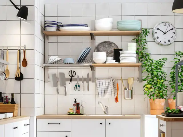 Una cocina pequeña y funcional con estantes llenos de vajilla, utensilios colgados y plantas verdes.