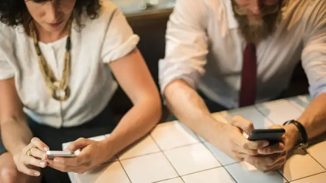 Zwei Personen sitzen an einem Tisch und schauen auf ihre Smartphones.