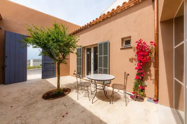Un patio andaluz con mesa y sillas de hierro forjado, un árbol frutal y buganvillas. Ideas para un oasis mediterráneo.