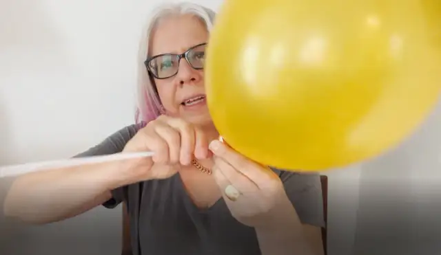 Kobieta w okularach mocuje żółty balon foliowy do białego patyka.