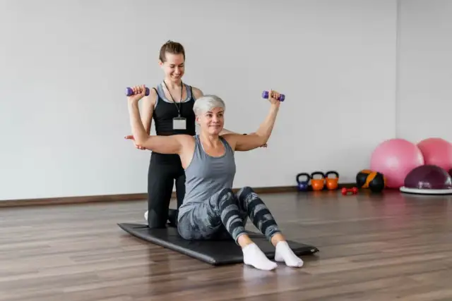 Fizjoterapeuta trener personalny wspiera kobietę w ćwiczeniach z hantlami.