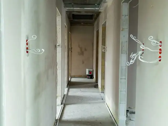 Korytarz w budowie. Widać przygotowane otwory pod puszki elektryczne z wystającymi przewodami. To ważny etap, co zrobić przed tynkami, by uniknąć późniejszych przeróbek.