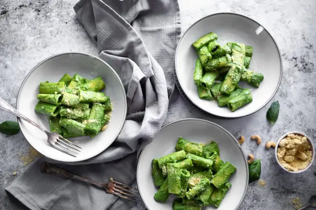 Drei Teller mit Rigatoni in cremiger, grüner veganer Spinatsoße, bestreut mit veganem Parmesan. Ein Genuss für Augen und Gaumen!