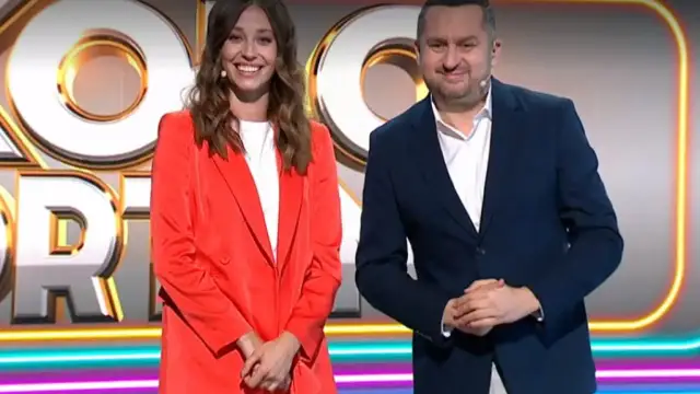Uśmiechnięta kobieta w czerwonej marynarce i mężczyzna w granatowym garniturze na tle logo "Koło Fortuny".