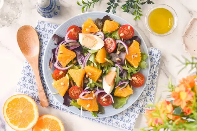 Ensalada de naranja vibrante con tomates cherry, huevo duro, cebolla morada y piñones. Una delicia fresca y colorida.