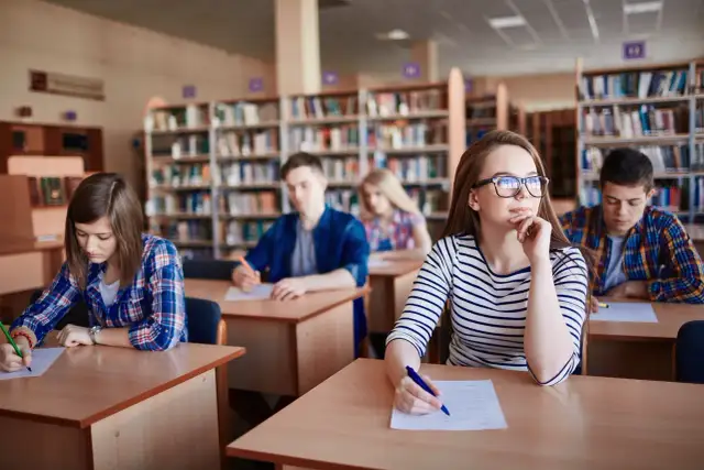 Uczniowie w bibliotece piszą test. Zastanawiają się, ile trwa szkoła zaoczna, gdy skupiają się na zadaniach.