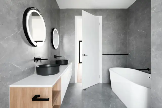 Elegante baño blanco y negro pequeño con lavabos negros, bañera exenta y espejos redondos iluminados.