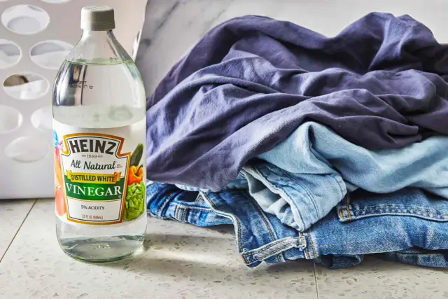Butelka octu do prania Heinz obok sterty niebieskich ubrań i dżinsów.