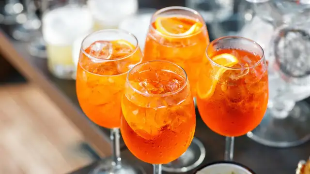 Cztery orzeźwiające drinki z aperolem i lodem, ozdobione plasterkami pomarańczy.