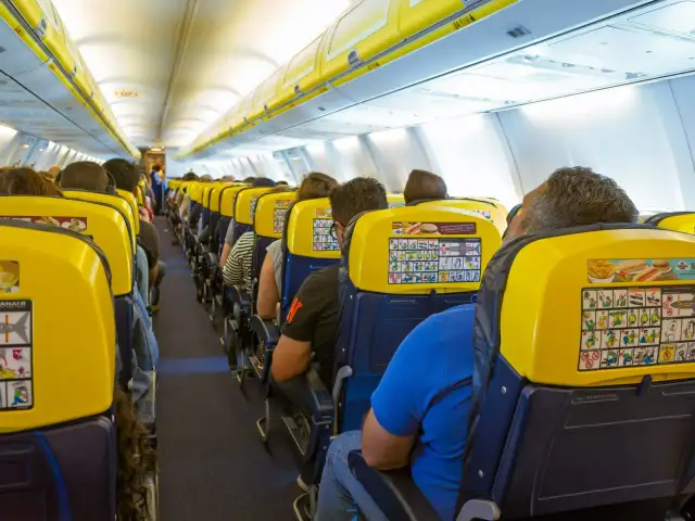 Wnętrze samolotu Ryanair z pasażerami siedzącymi w żółtych fotelach.