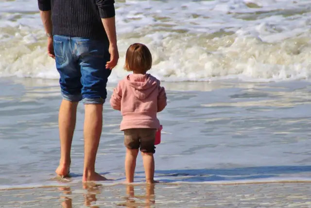 Ojciec i dziecko na plaży, cieszący się wspólnym urlopem ojcowskim 9 tygodni.