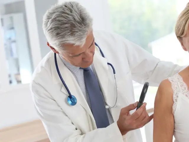 Lekarz bada skórę pacjentki. Czy do dermatologa trzeba mieć skierowanie od lekarza rodzinnego? Sprawdź!
