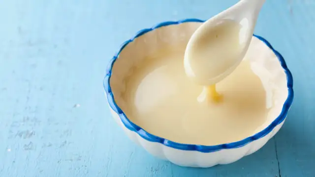 Cuchara con leche evaporada, un ingrediente cremoso y dulce, ideal para postres.
