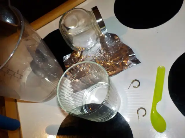 Szklanka, folia aluminiowa, sól, łyżeczka i kolczyki na blacie.